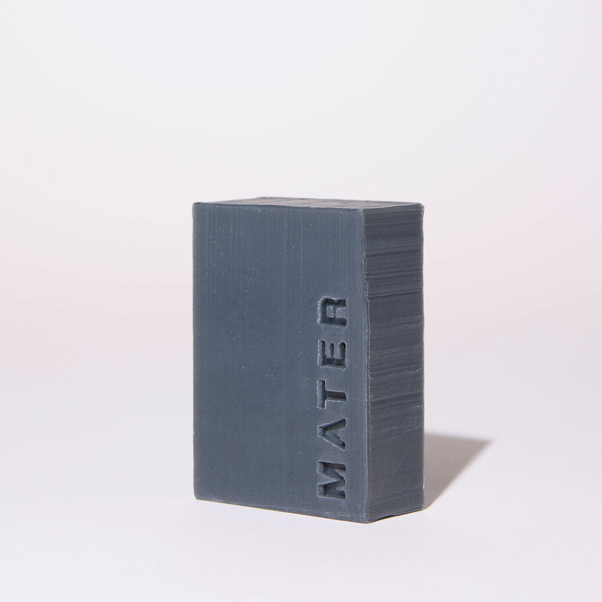 A rectangular dark gray bar of soap standing upright on a white background, with the brand name 'MATER' embossed vertically on the front face.