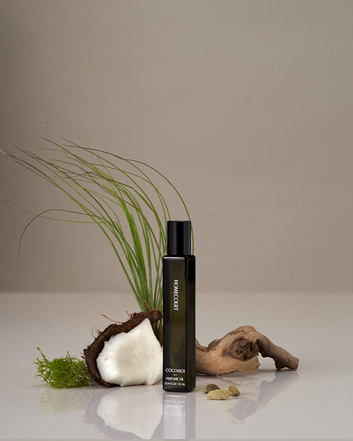 Homecourt Cocomoi Perfume Oil black bottle with greenery and coconut on a neutral background