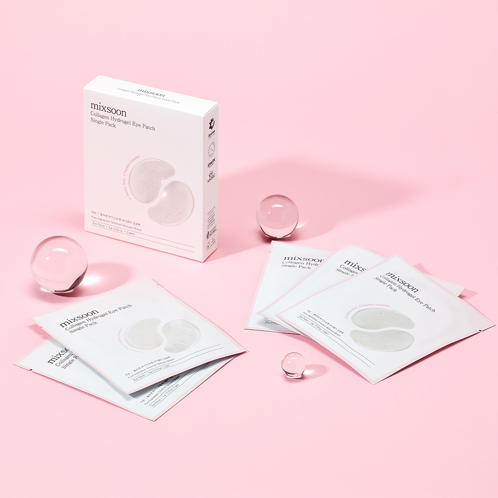 mixsoon Collagen Hydrogel Eye Patch Single Pack packaging and individual sachets arranged on a soft pink background with clear glass spheres. The box and packets are white with pale gray printed eye patch imagery and the mixsoon brand name visible.