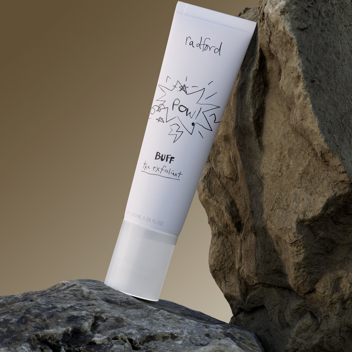 A white tube of Radford Buff the Exfoliant stands upright against large textured rocks, with a warm beige gradient background.
