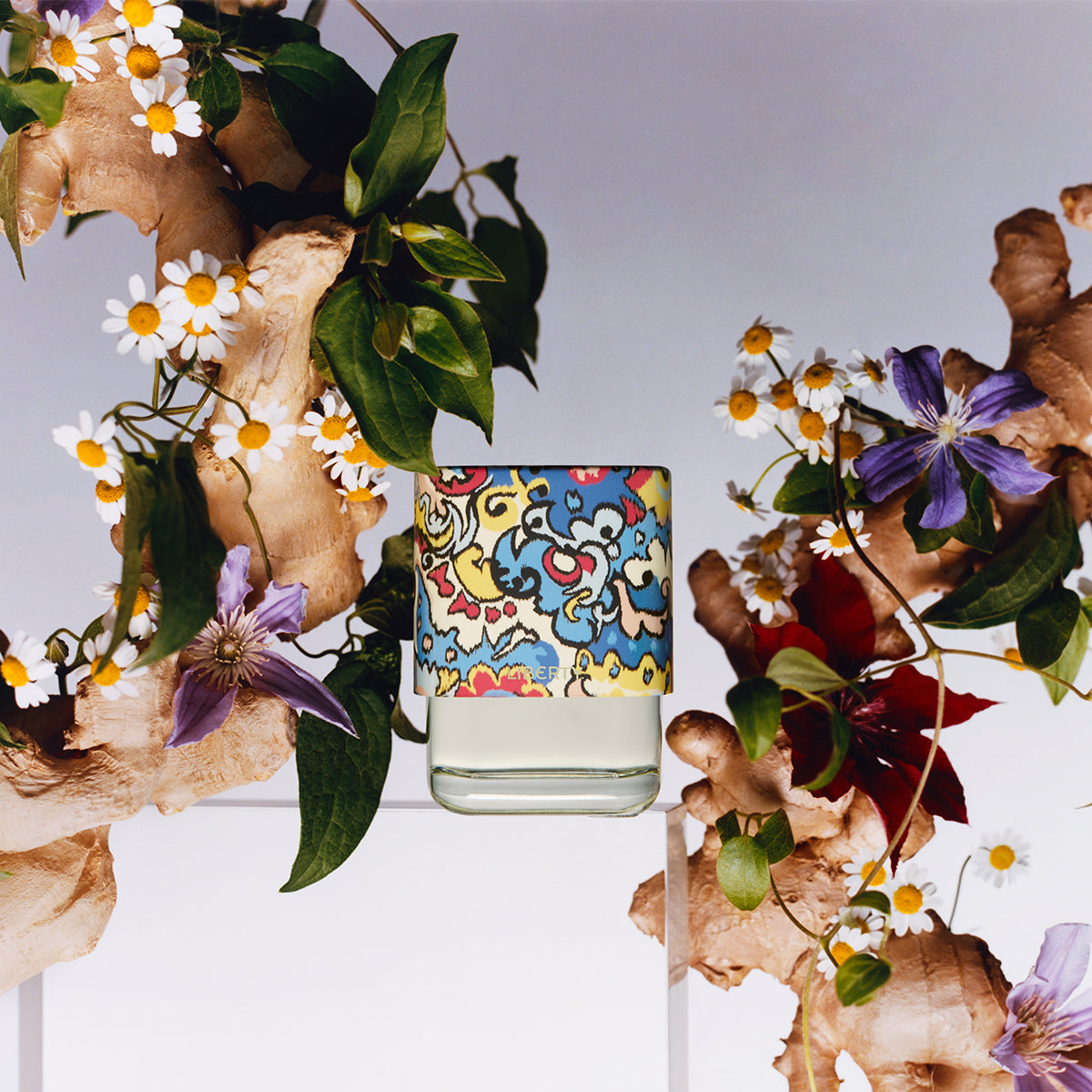 Perfume bottle with colorful design surrounded by flowers and leaves on a white background