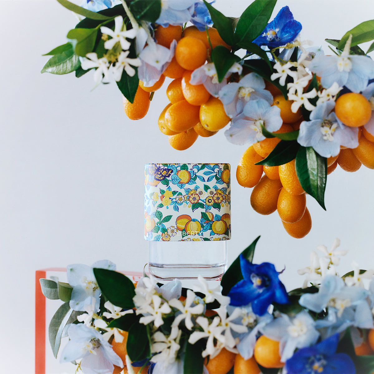 Decorative arrangement of oranges, flowers, and Liberty Perfume bottle on a white background