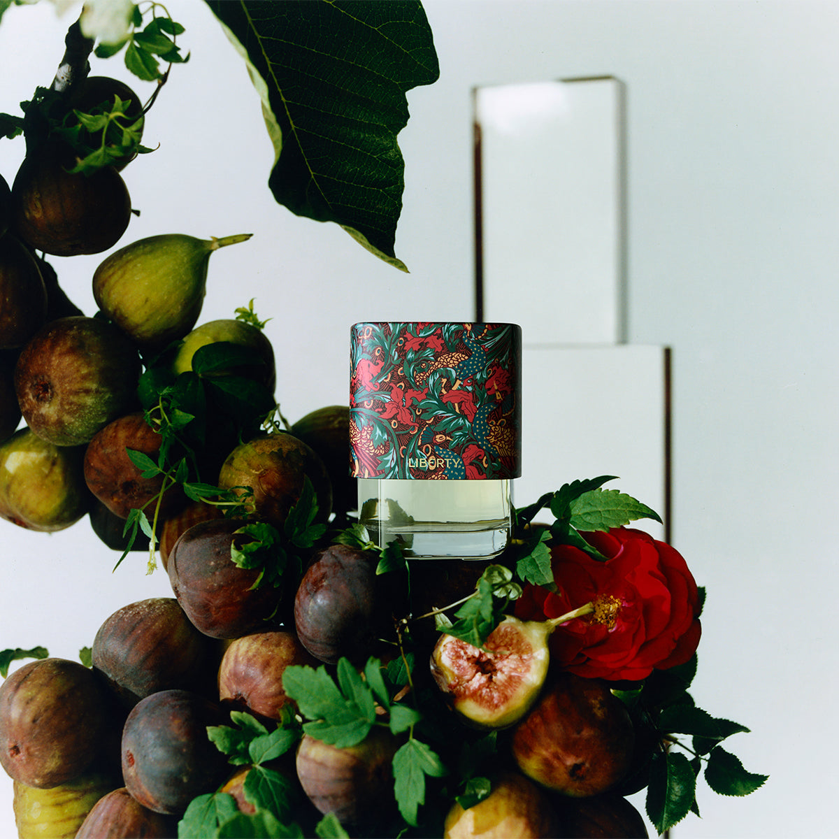Perfume bottle with floral design surrounded by figs and flowers on a white background