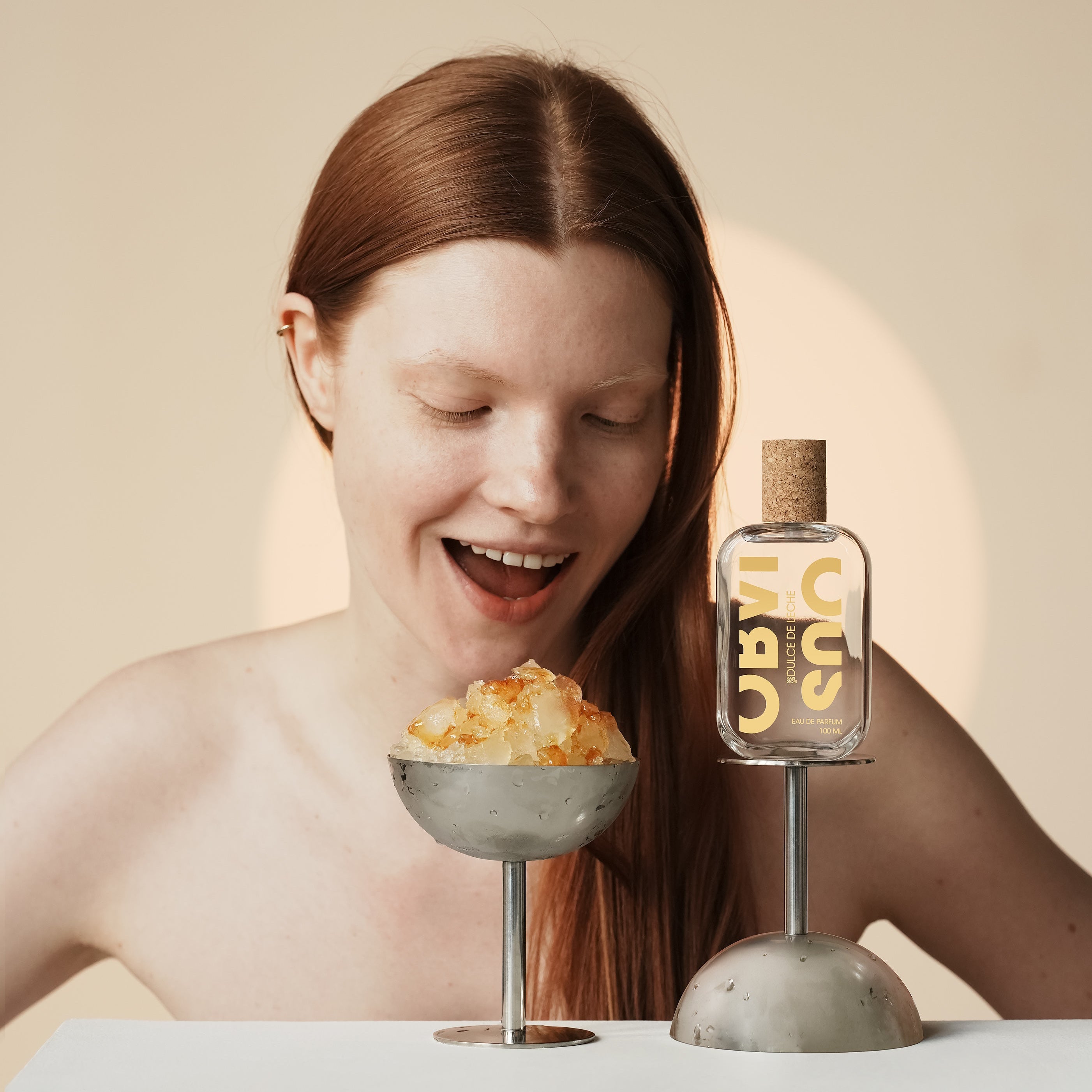 Woman with a glass of orange ice and a bottle of perfume on a beige background