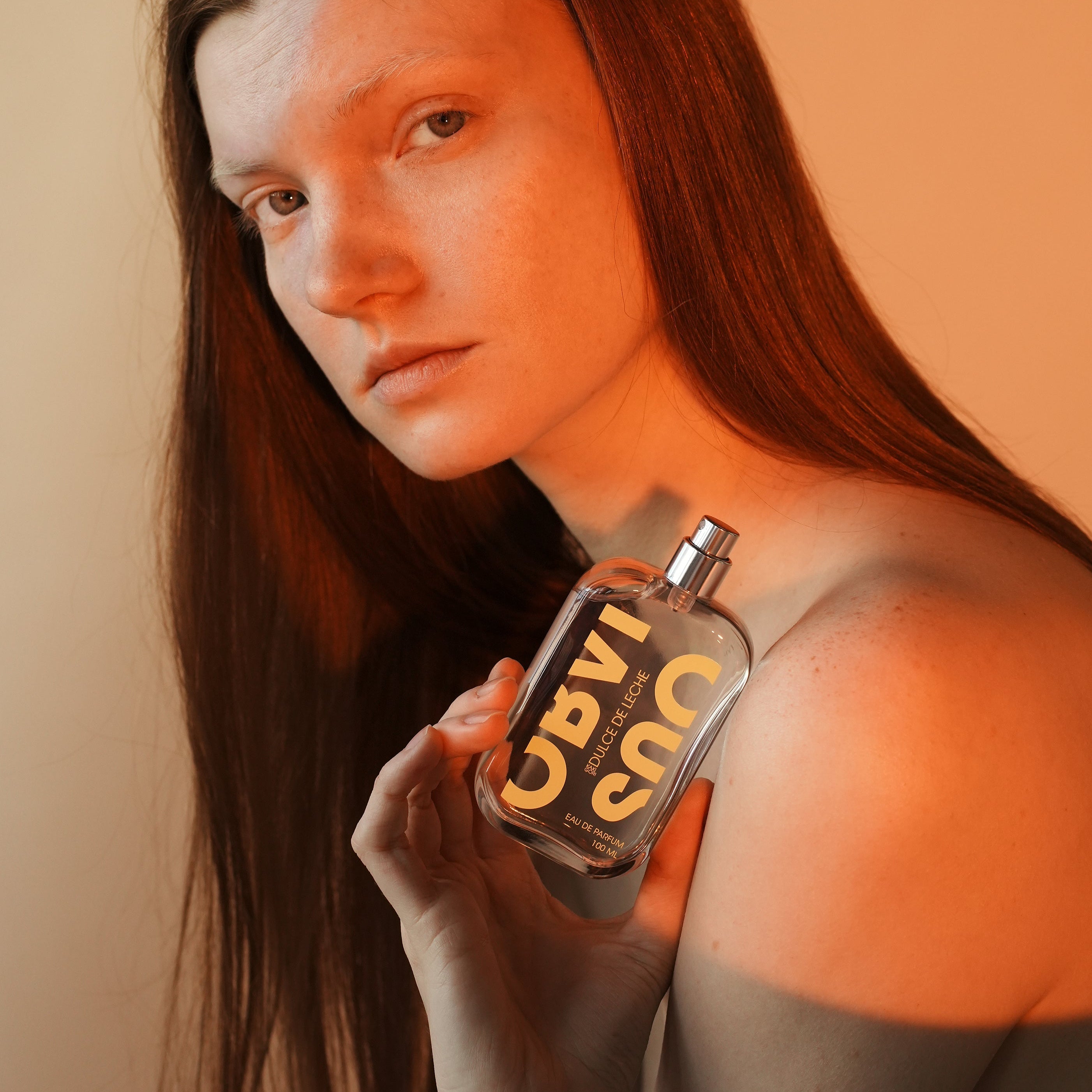 Woman holding a bottle of perfume in warm light against a plain background