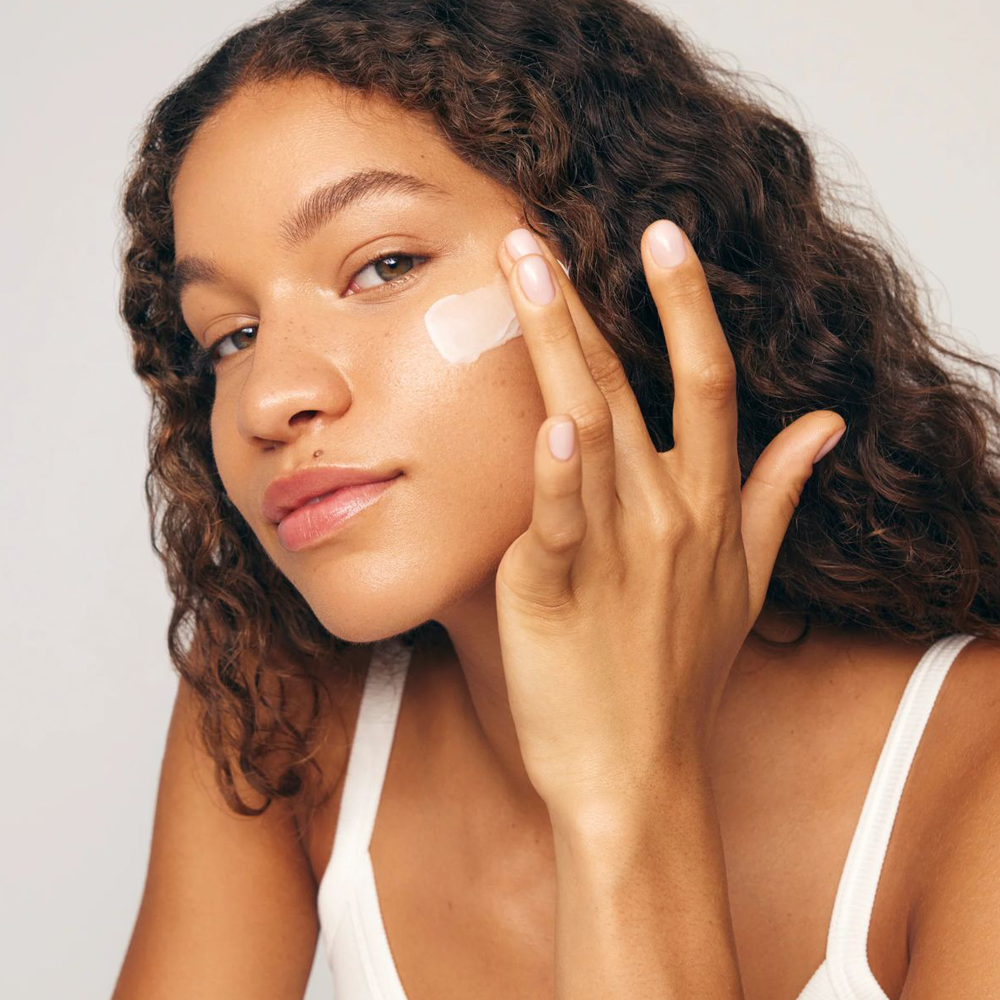 Woman applying cream to her face with a neutral background