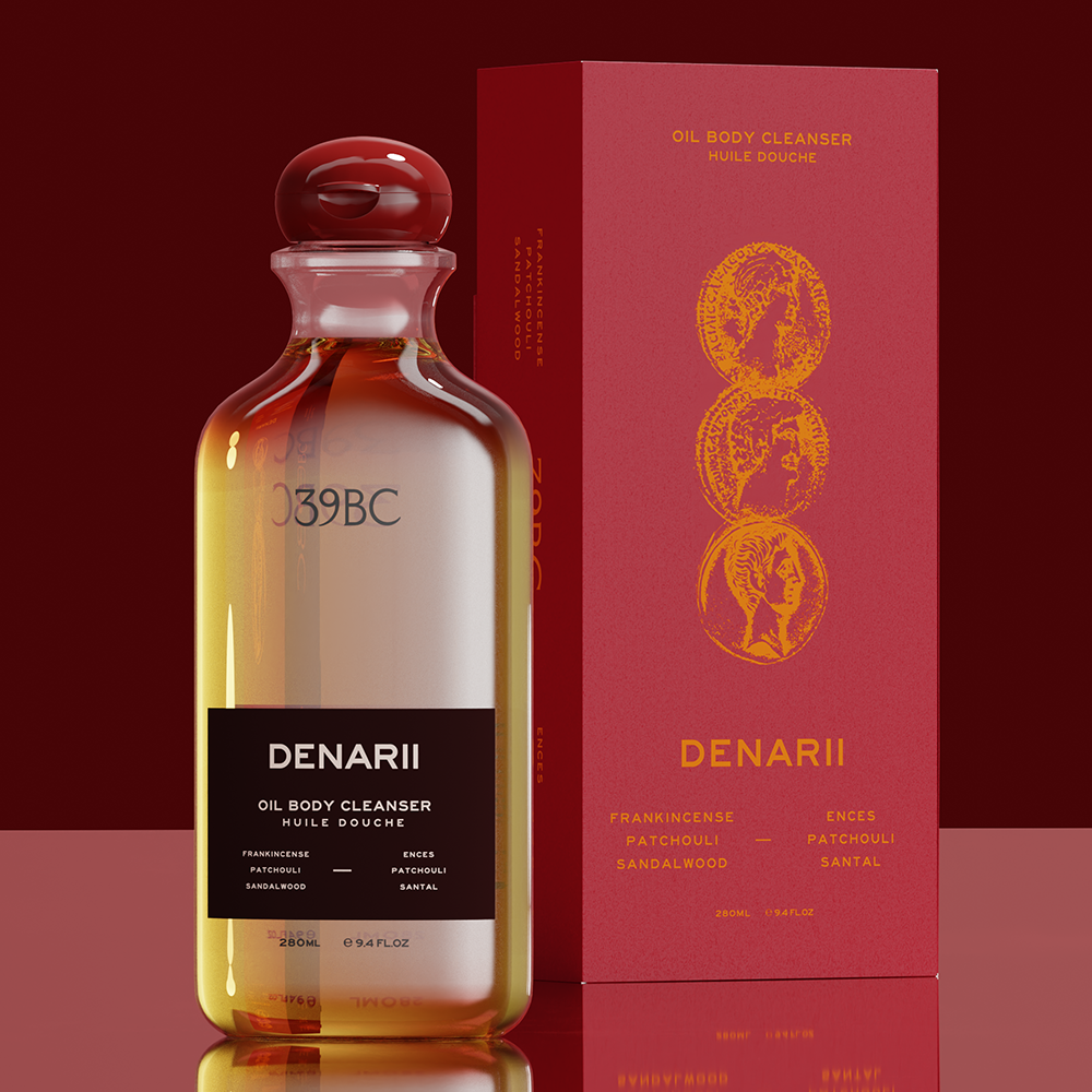 Bottle of 39BC Denarii Oil Body Cleanser beside a tall red box with gold circular illustrations and gold text, on a dark red background.