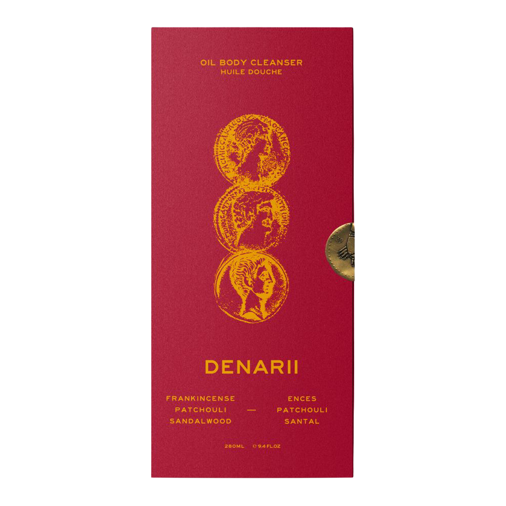A tall, narrow red box for 39BC Denarii Oil Body Cleanser, featuring gold text and three gold coin illustrations on the front, with a small round gold seal on the right side, photographed against a plain white background.