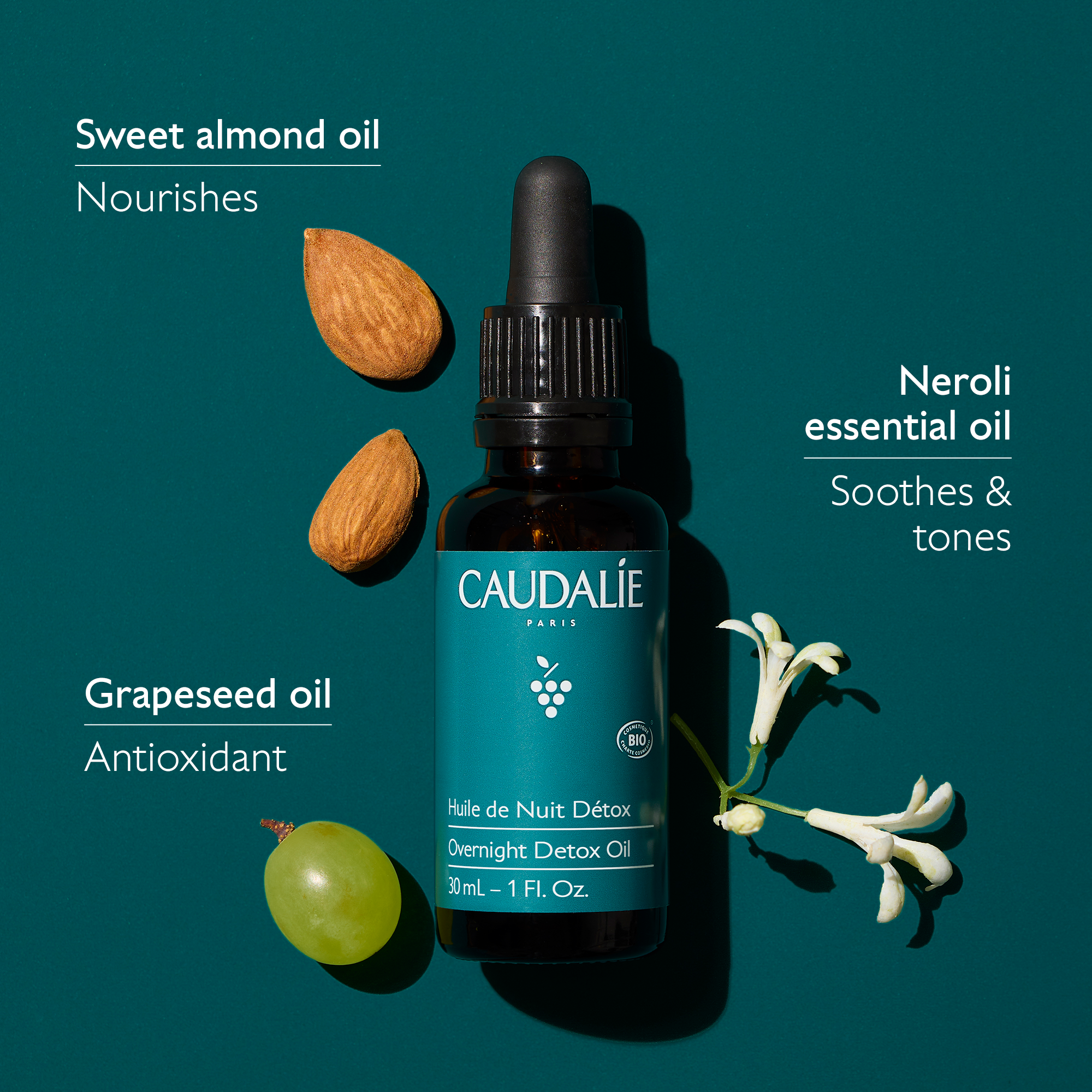Caudalie skincare oil bottle with almonds, grapes, and neroli essential oil on a dark green background
