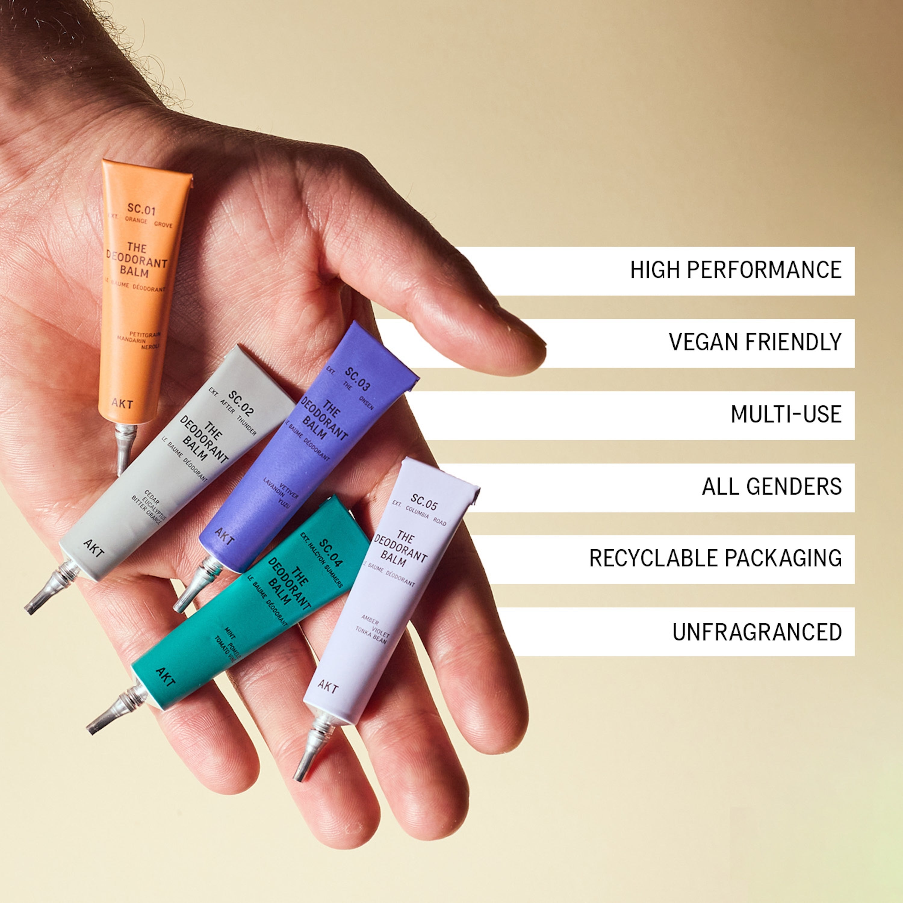 A hand holds five tubes of AKT 'The Deodorant Balm' against a warm beige background, with text callouts listing product benefits: high performance, vegan friendly, multi-use, all genders, recyclable packaging, and unfragranced. 