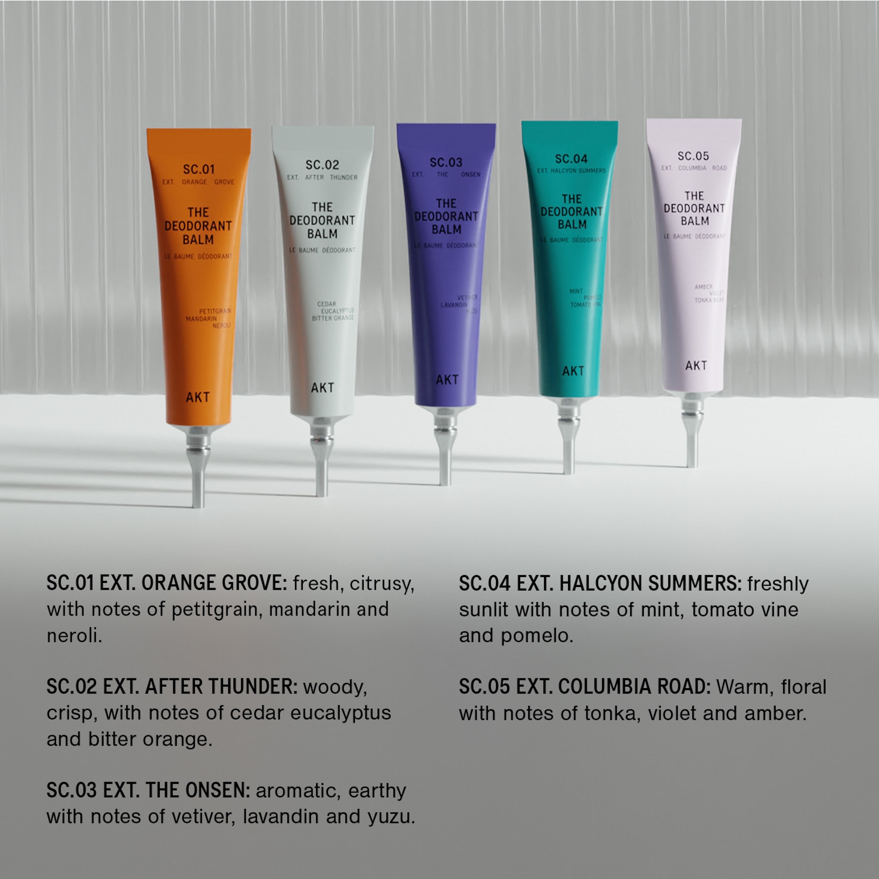 Five tubes of AKT 'The Deodorant Balm' lined up against a gray background, with scent descriptions printed below.