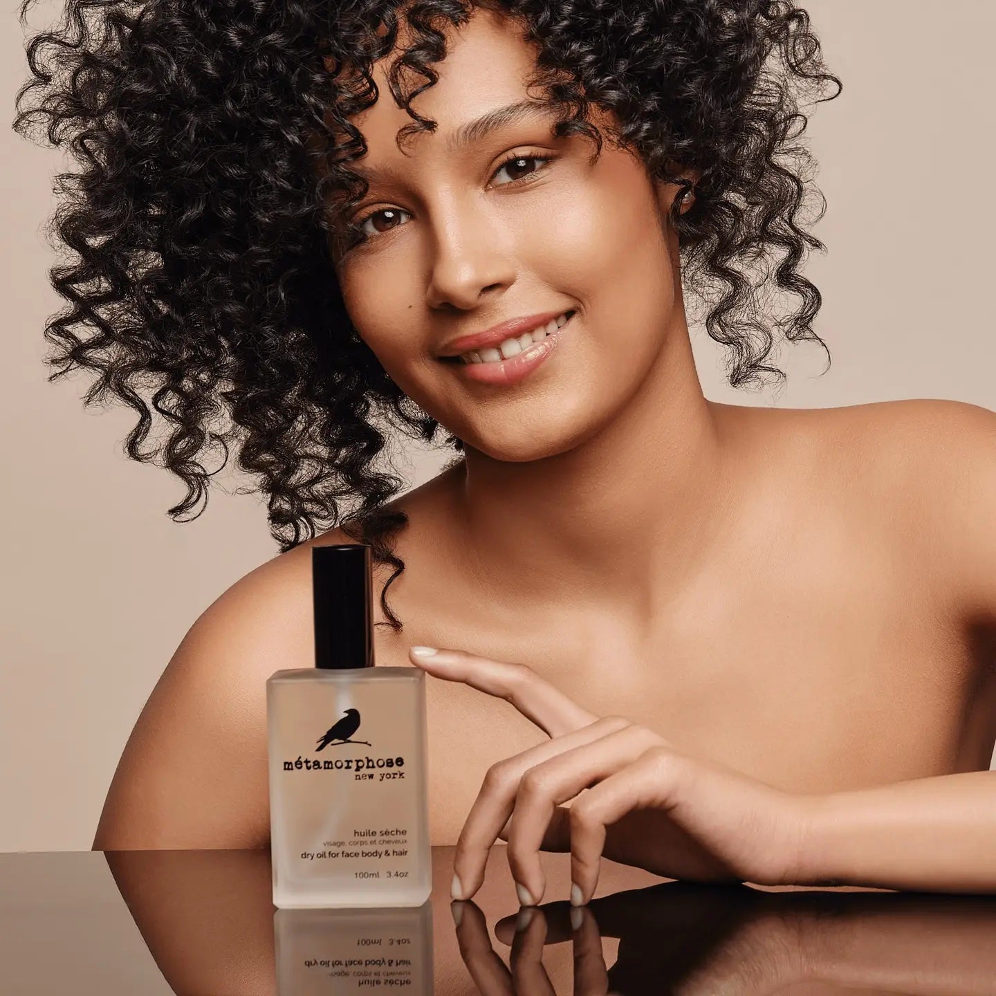 Woman holding a bottle of 'Metamorphose' Dry Oil with a neutral background