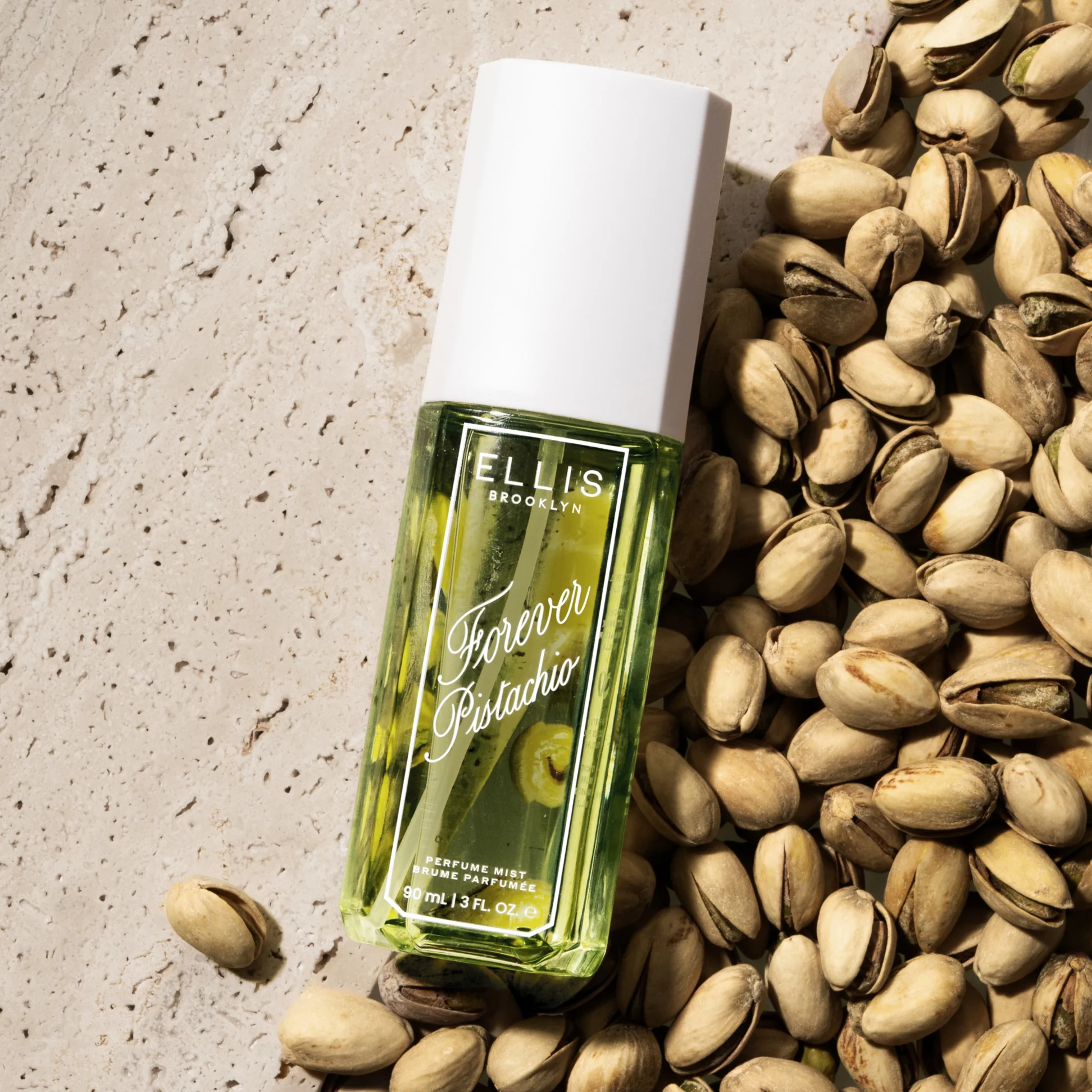 Bottle of Ellis Brooklyn Forever Pistachio perfume surrounded by pistachios on a textured surface