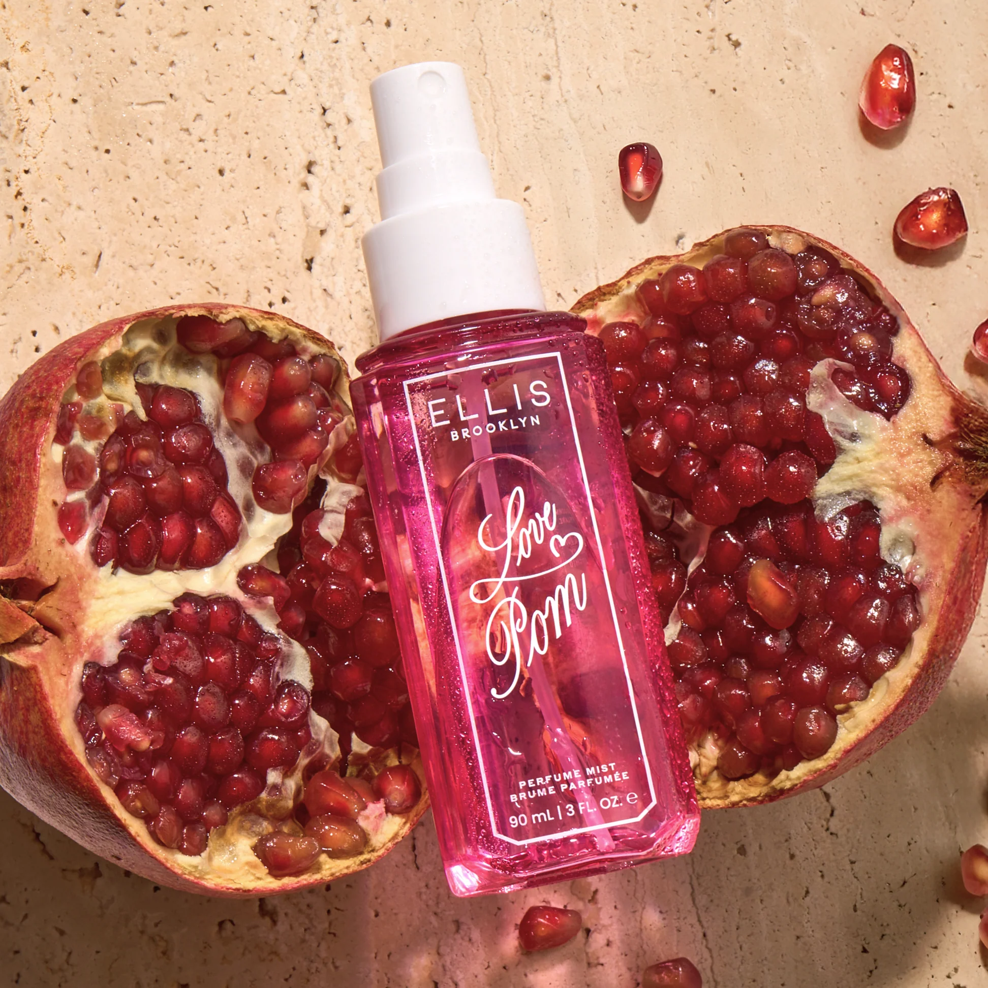 Perfume bottle with 'Love Pom' text surrounded by pomegranate fruits on a textured surface