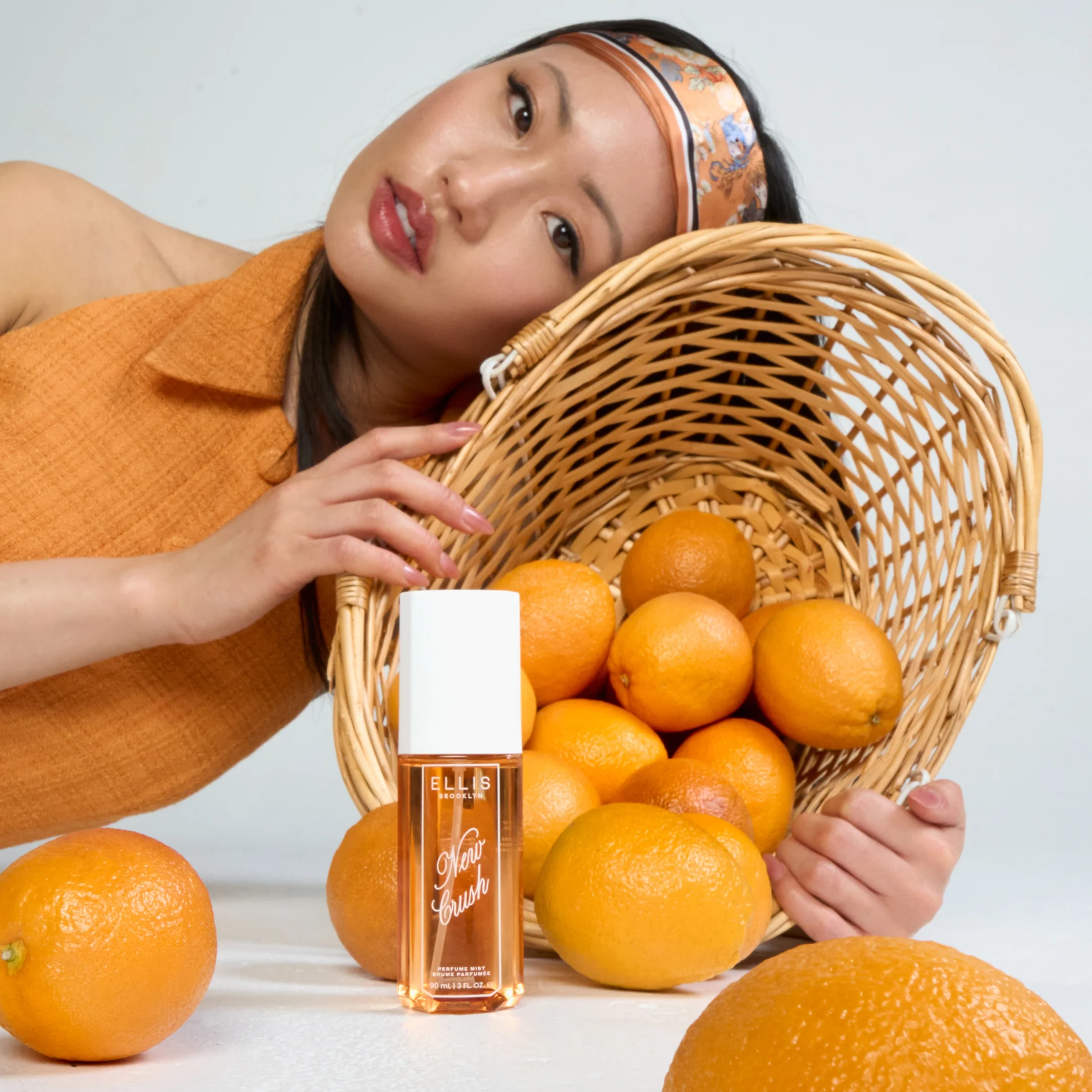 Woman holding a basket of oranges with a bottle of perfume in front