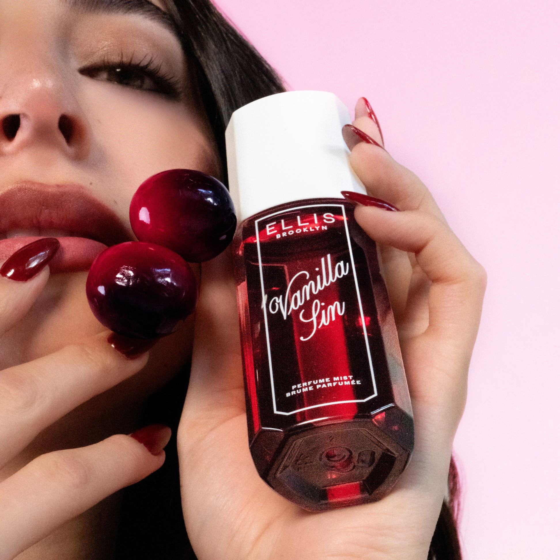 Hand holding a red Ellis Brooklyn Vanilla Sin perfume bottle with a pink background