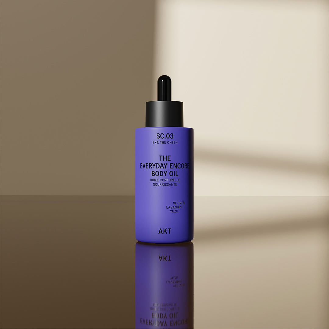 AKT The Everyday Encore Body Oil Sc.03 on a reflective surface in front of a beige background