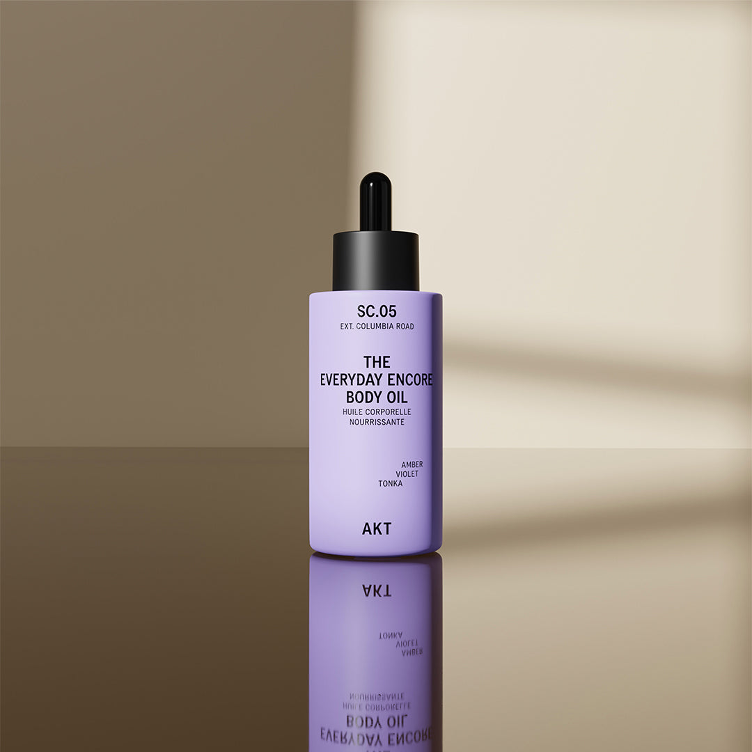 AKT The Everyday Encore Body Oil Sc.05 bottle on a reflective surface and neutral background