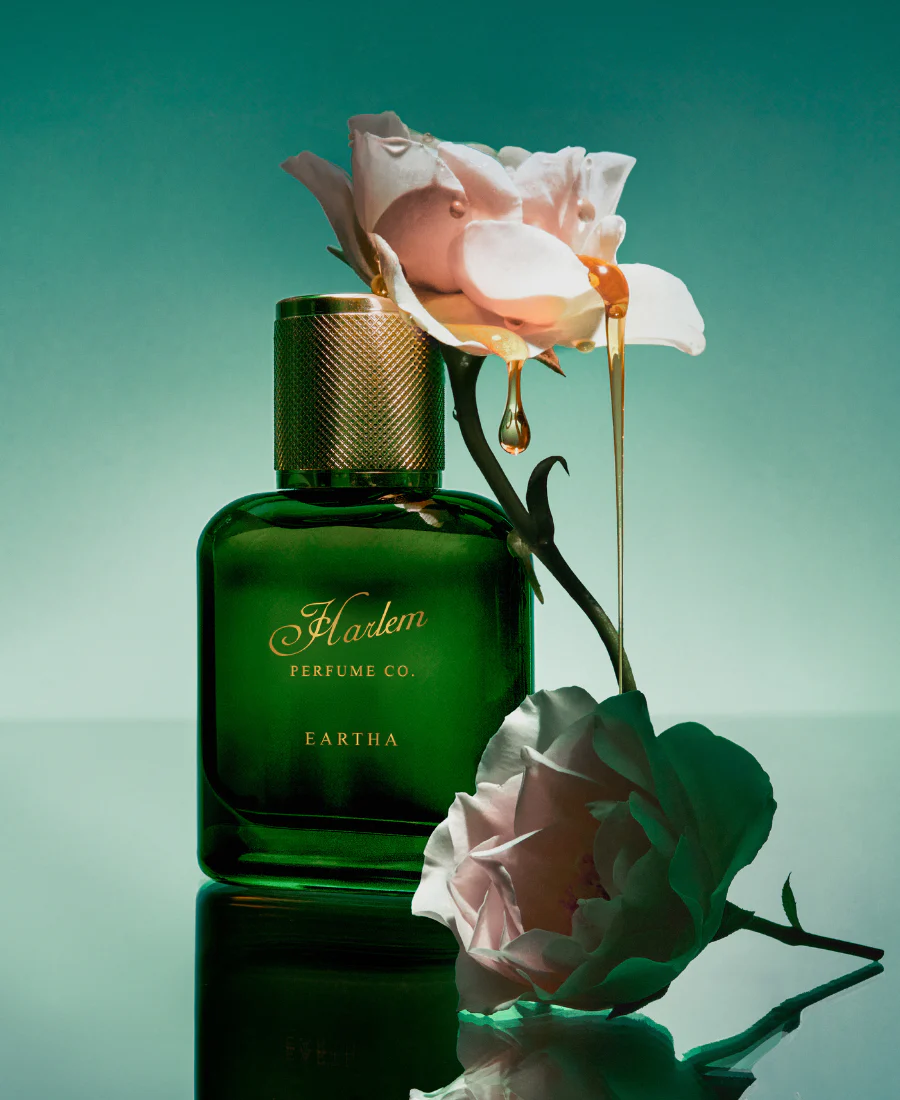 Green perfume bottle with gold cap and pink flowers on a reflective surface
