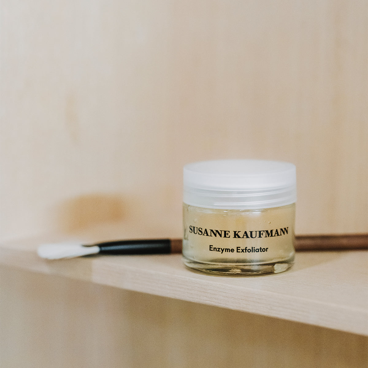 Jar of Susanne Kaufmann Enzyme Exfoliator on a wooden shelf with a blurred background