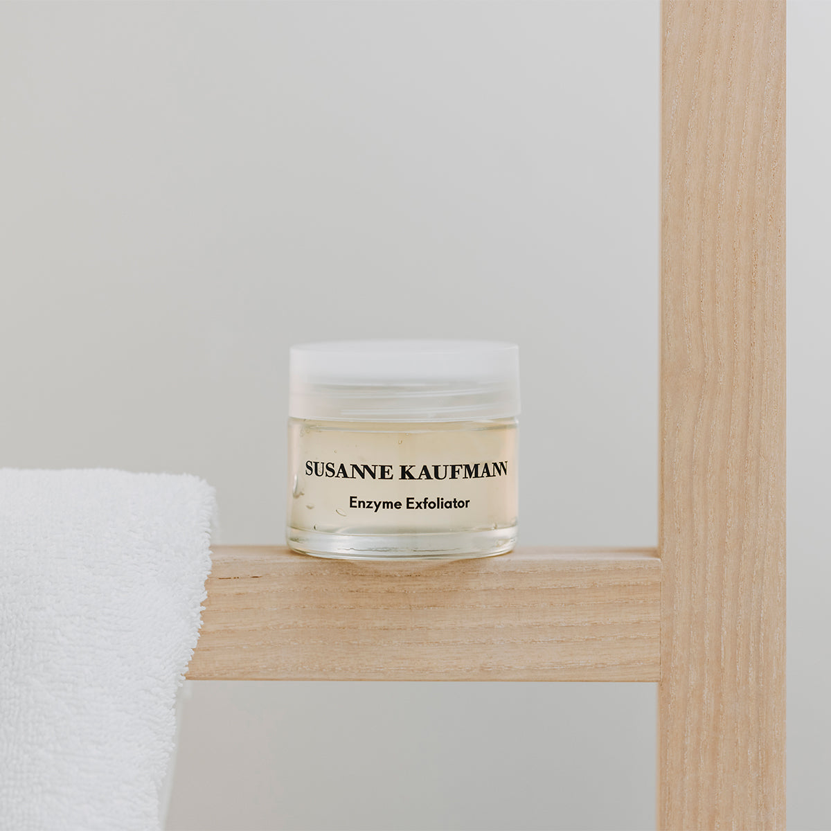 Susanne Kaufmann Enzyme Exfoliator jar on a wooden shelf with a white towel.