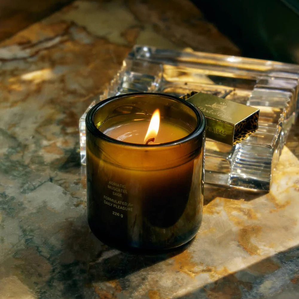 Flamingo Estate Candle in a glass holder on a marble surface with a lighter next to it
