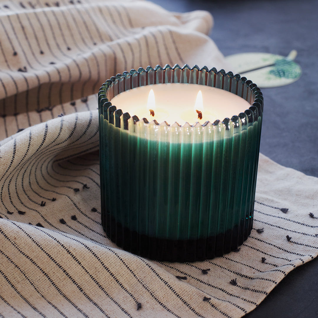 Roland Pine Green candle in a textured glass holder on a patterned fabric surface