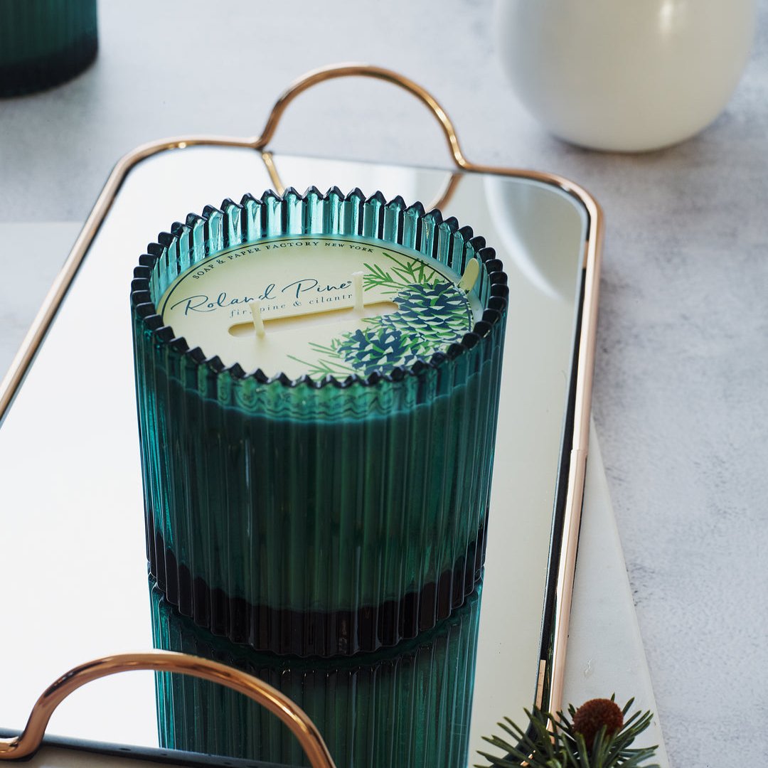 Green glass 2-wick candle sitting on a mirror tray on a countertop.