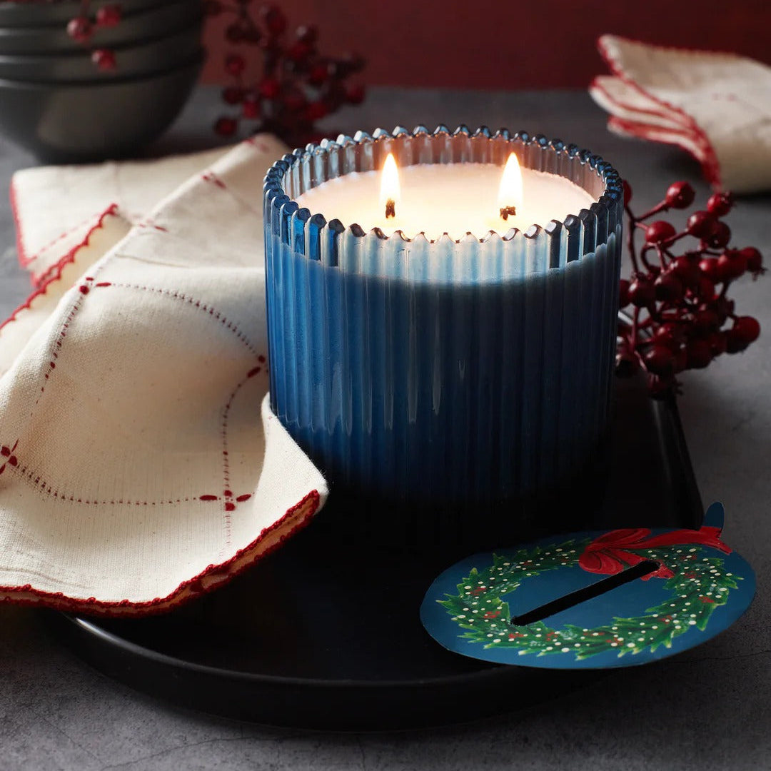 Roland Pine Blue candle with a festive design  on a dark surface with decorative elements.