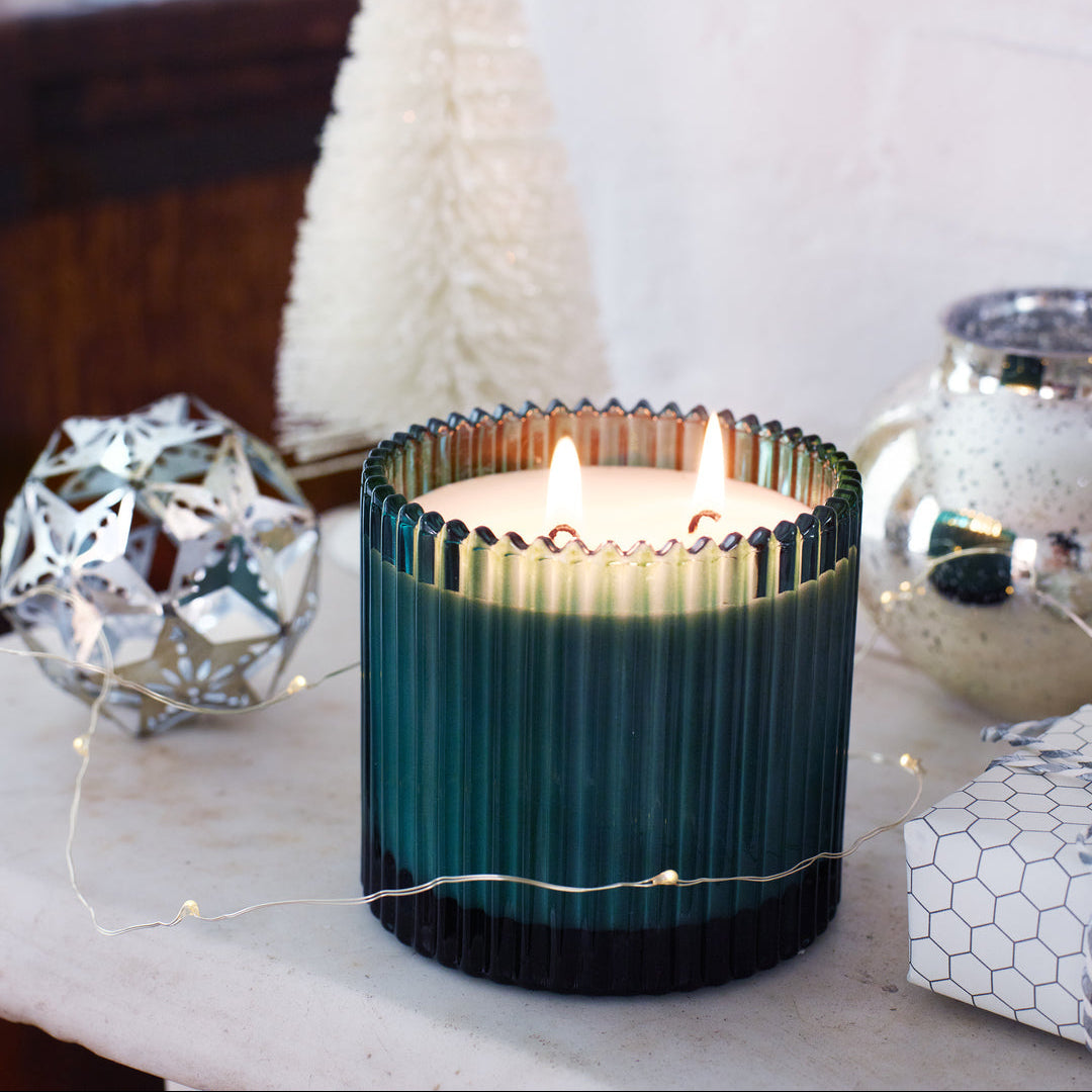 Roland pine candle in a ribbed container on a surface with decorative items in the background