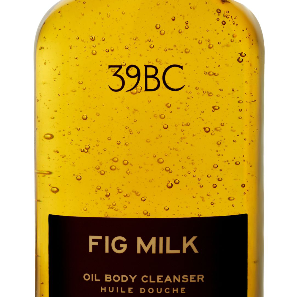 A close-up of a 39BC Fig Milk Oil Body Cleanser bottle, showing golden yellow translucent liquid with visible air bubbles and a black label at the bottom.