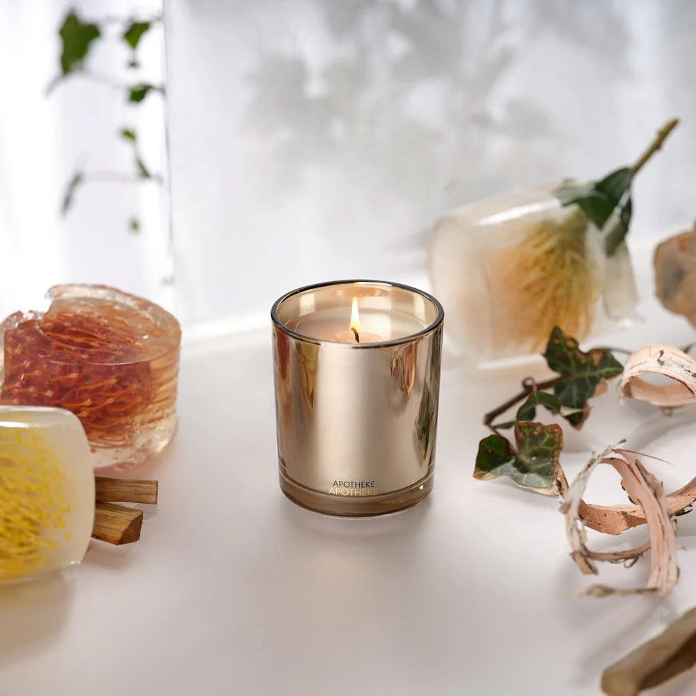 A lit candle in a gold jar surrounded by decorative items on a white surface.