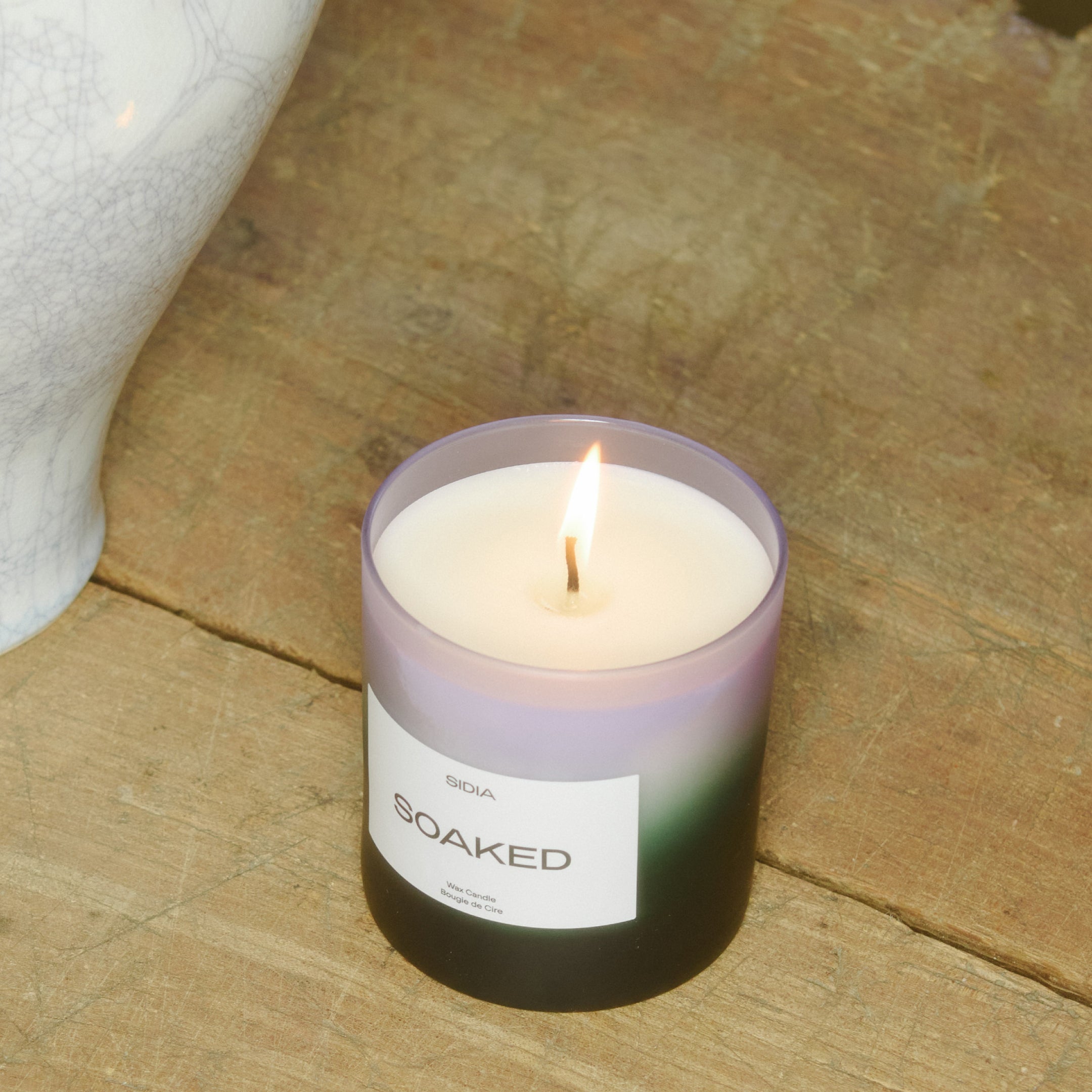SIDIA candle in "SOAKED" scent on a wood floor
