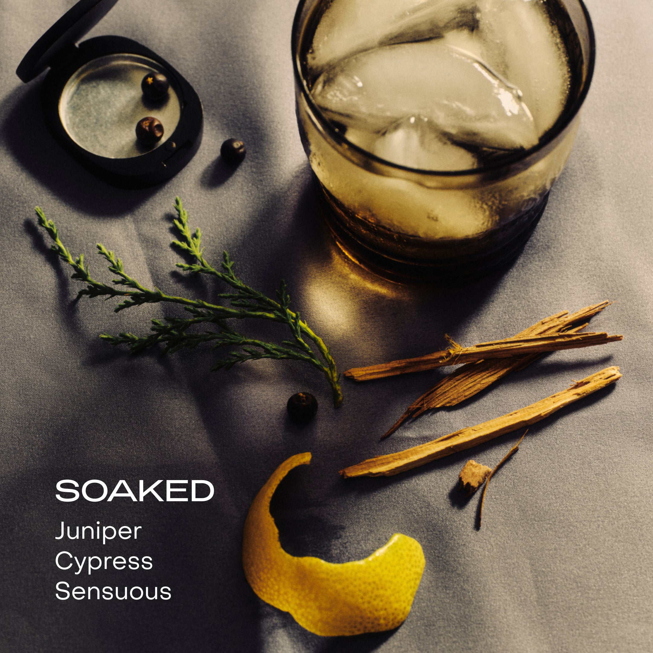 A glass with ice, an orange peel. and an herb on a cloth background