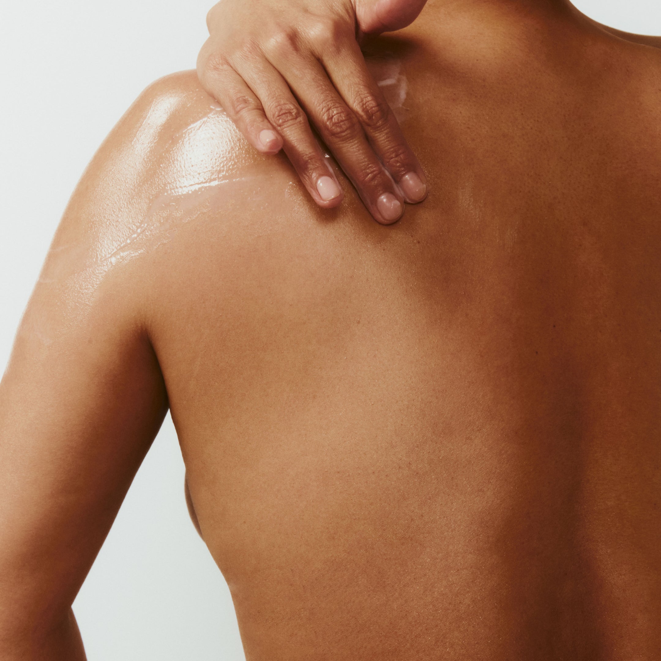 Person applying a skincare product to their shoulder with a neutral background