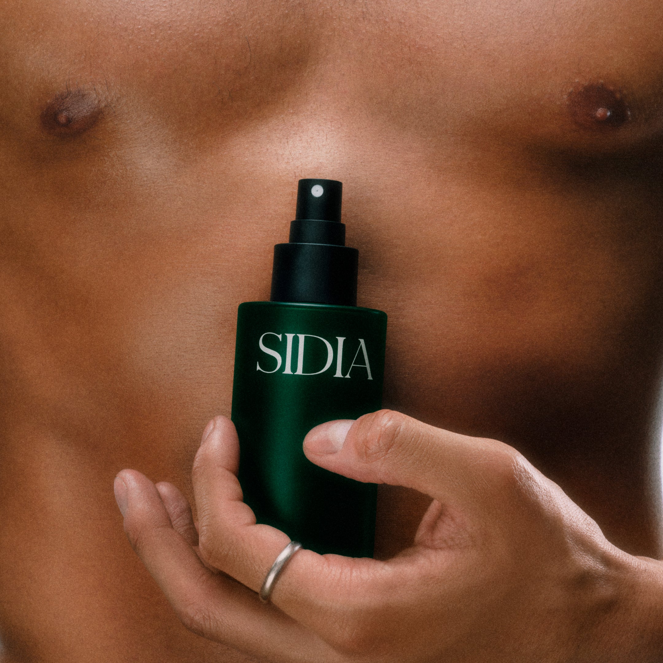 Person holding a Sidia spray bottle against a skin background