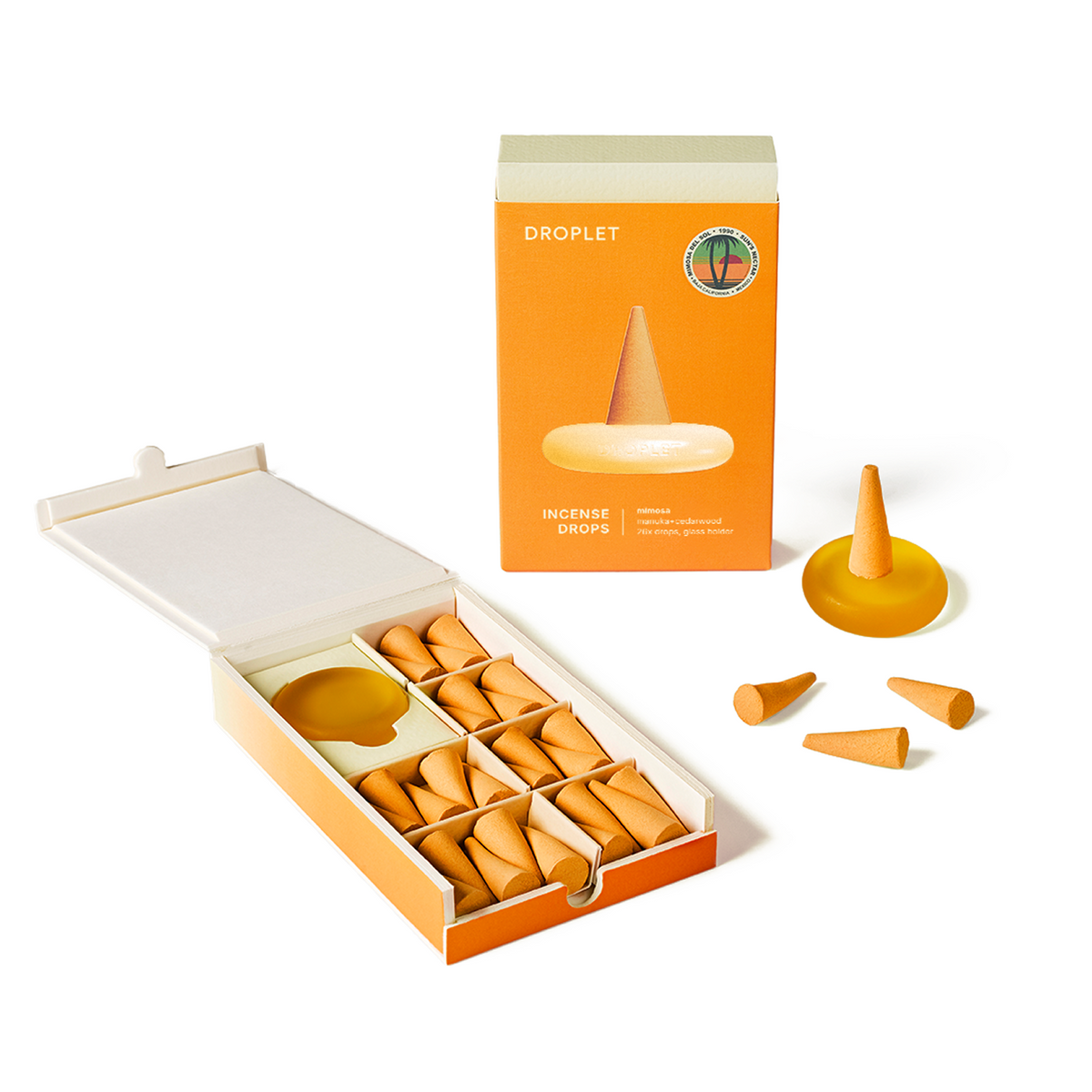 An open orange and white box of droplet incense drops with multiple small orange cone-shaped incense pieces arranged in compartments, plus a few loose incense pieces and a matching orange product box on a clean white background.