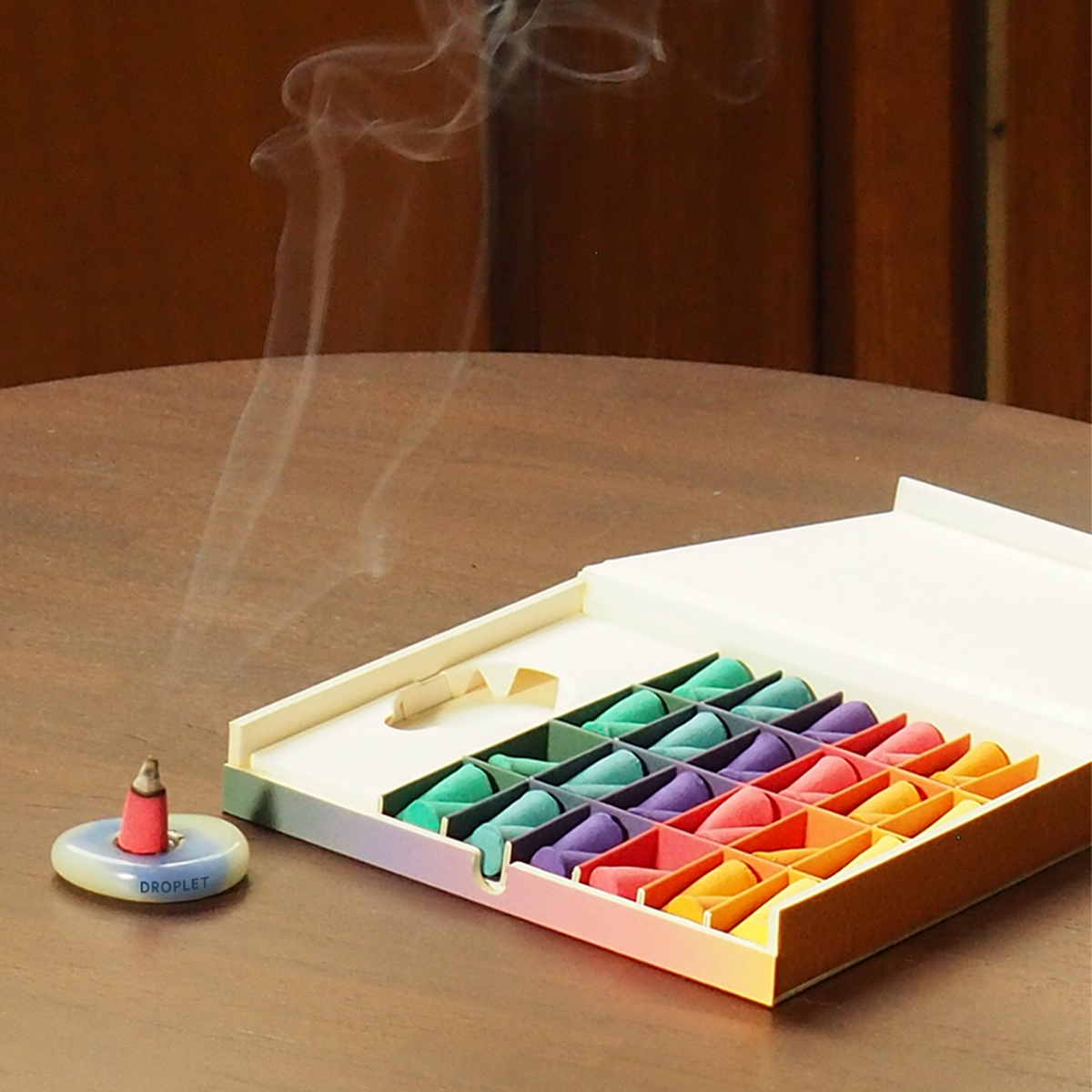 Colorful incense sticks in an open box with a lit incense stick on a wooden surface.