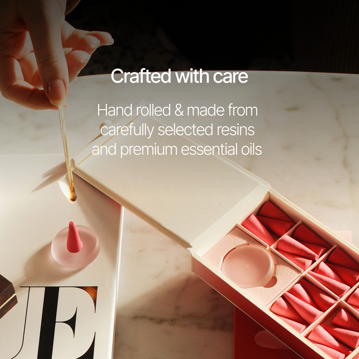 A hand is shown rolling a small pink conical item over a wooden surface next to an open box filled with similar pink rolled pieces. White text on the image reads, 'Crafted with care' and 'Hand rolled & made from carefully selected resins and premium essential oils.