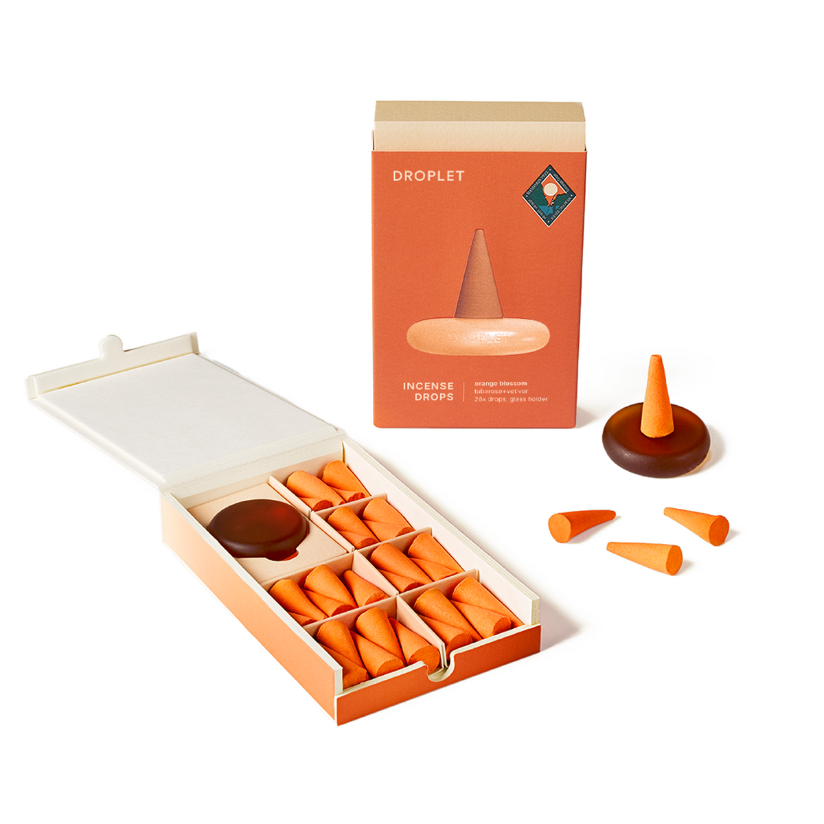 An open orange and cream box of Droplet incense drops, showing multiple small orange cone-shaped incense pieces and a dark brown incense burner, with the matching product box standing behind on a white background.