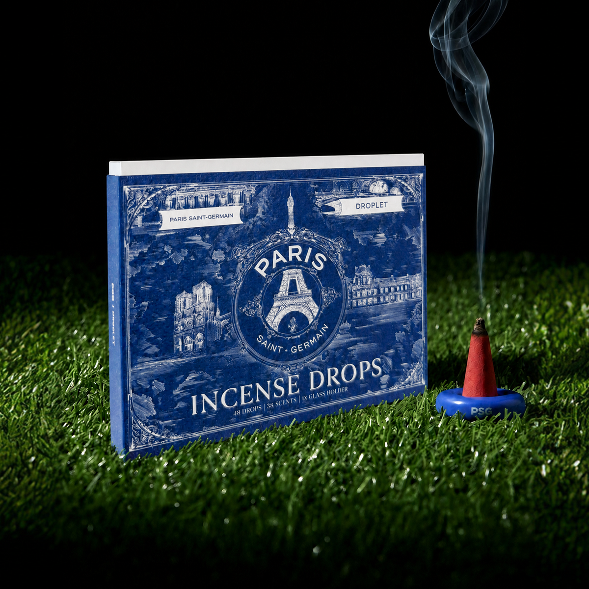 Blue box of 'Paris Saint-Germain' incense drops with a red cone and smoke on grass
