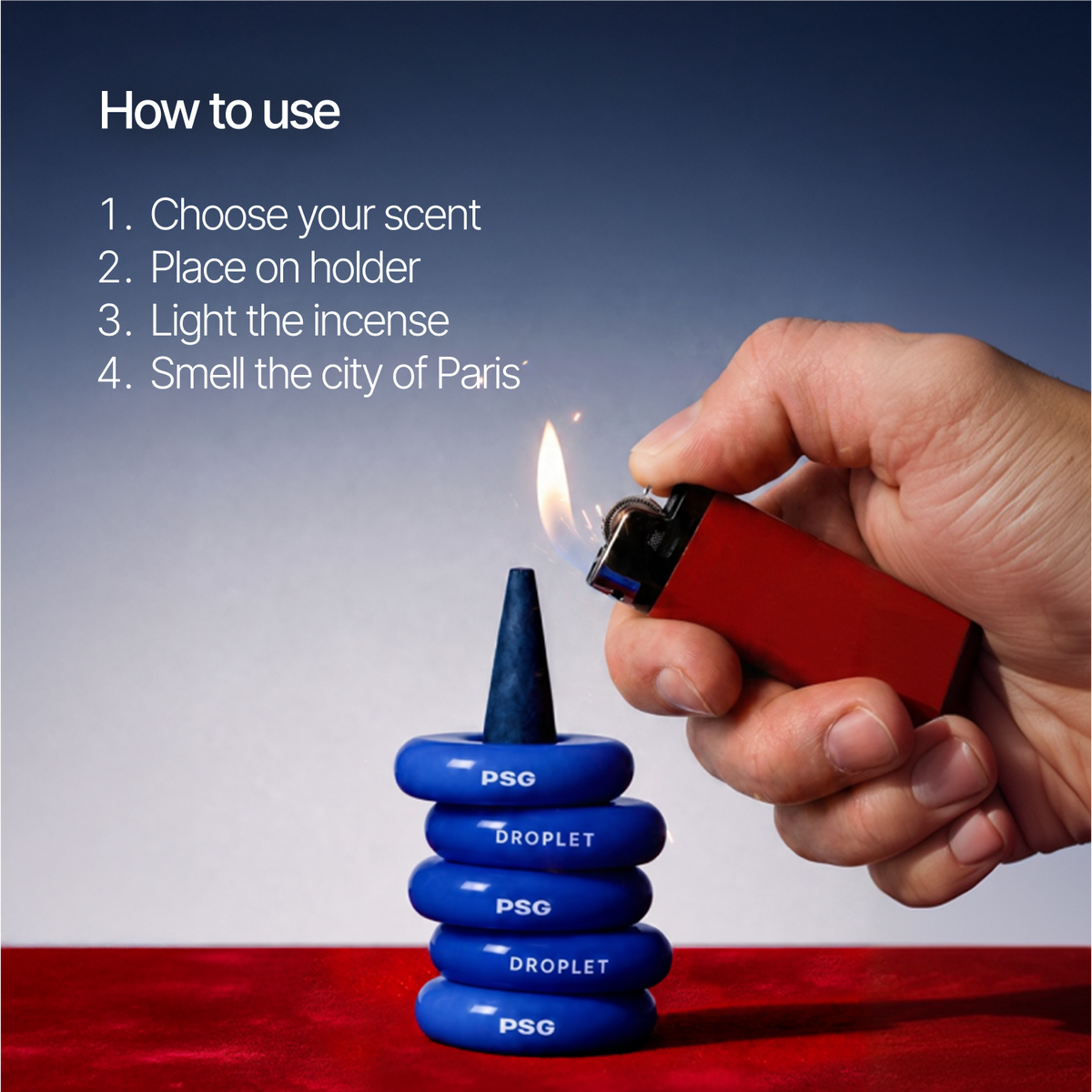 A hand holds a red lighter over a stack of blue droplet-shaped incense pieces labeled PSG and DROPLET, with a flame burning the top cone. White text on the left reads 'How to use' with four steps, including choosing scent and smelling the city of Paris.