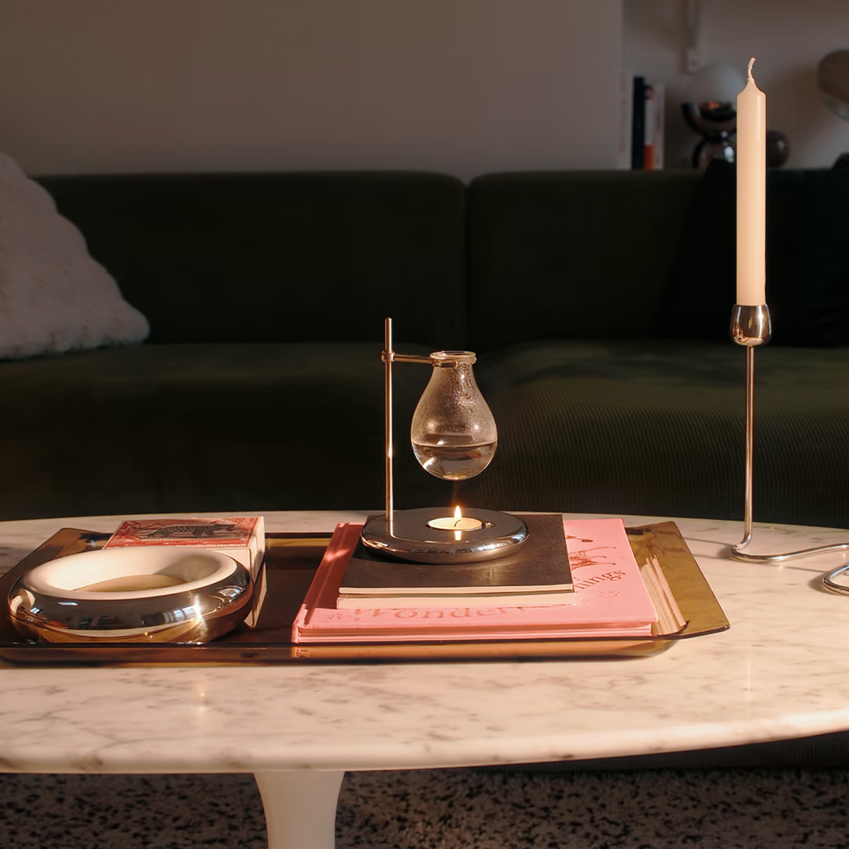 Droplet Burner along decorative items on a marble table with a dark sofa in the background