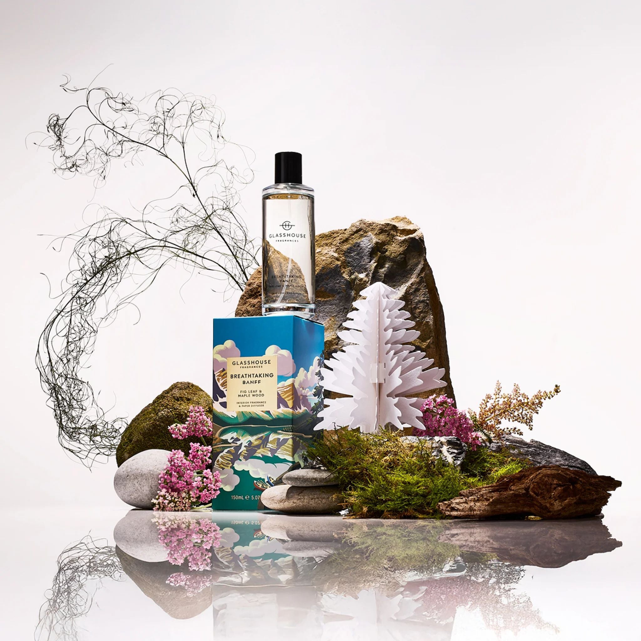 Cosmetic products on a natural setting with rocks, plants, and flowers.