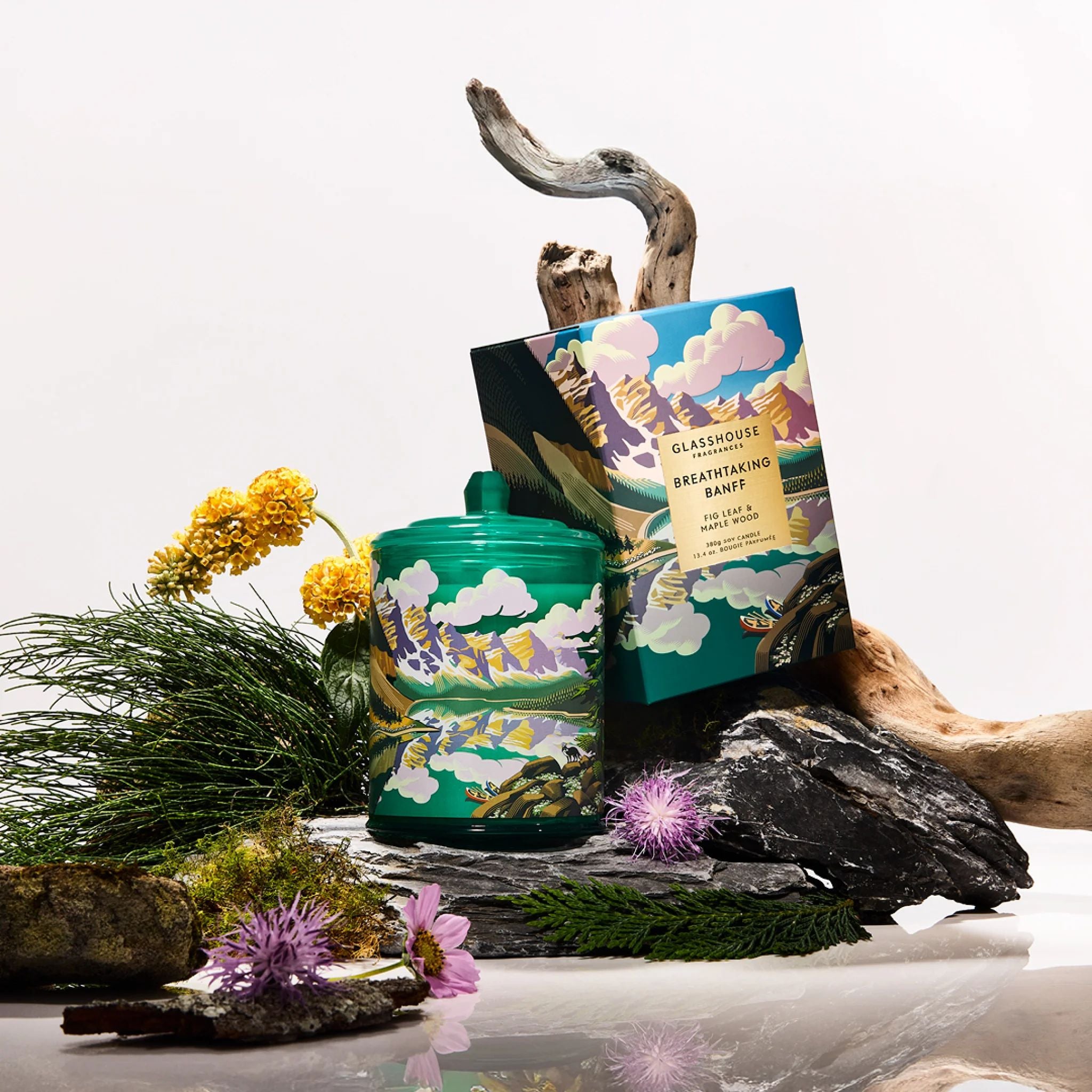 Candle with decorative packaging on a natural setting with flowers and rocks