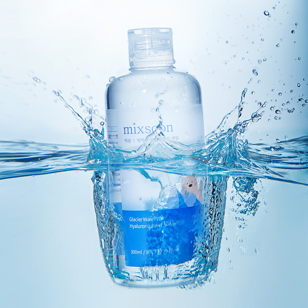 A clear plastic bottle of Mixsoon Glacier Water Hyaluronic Acid Serum floating in splashing blue water against a light blue background.