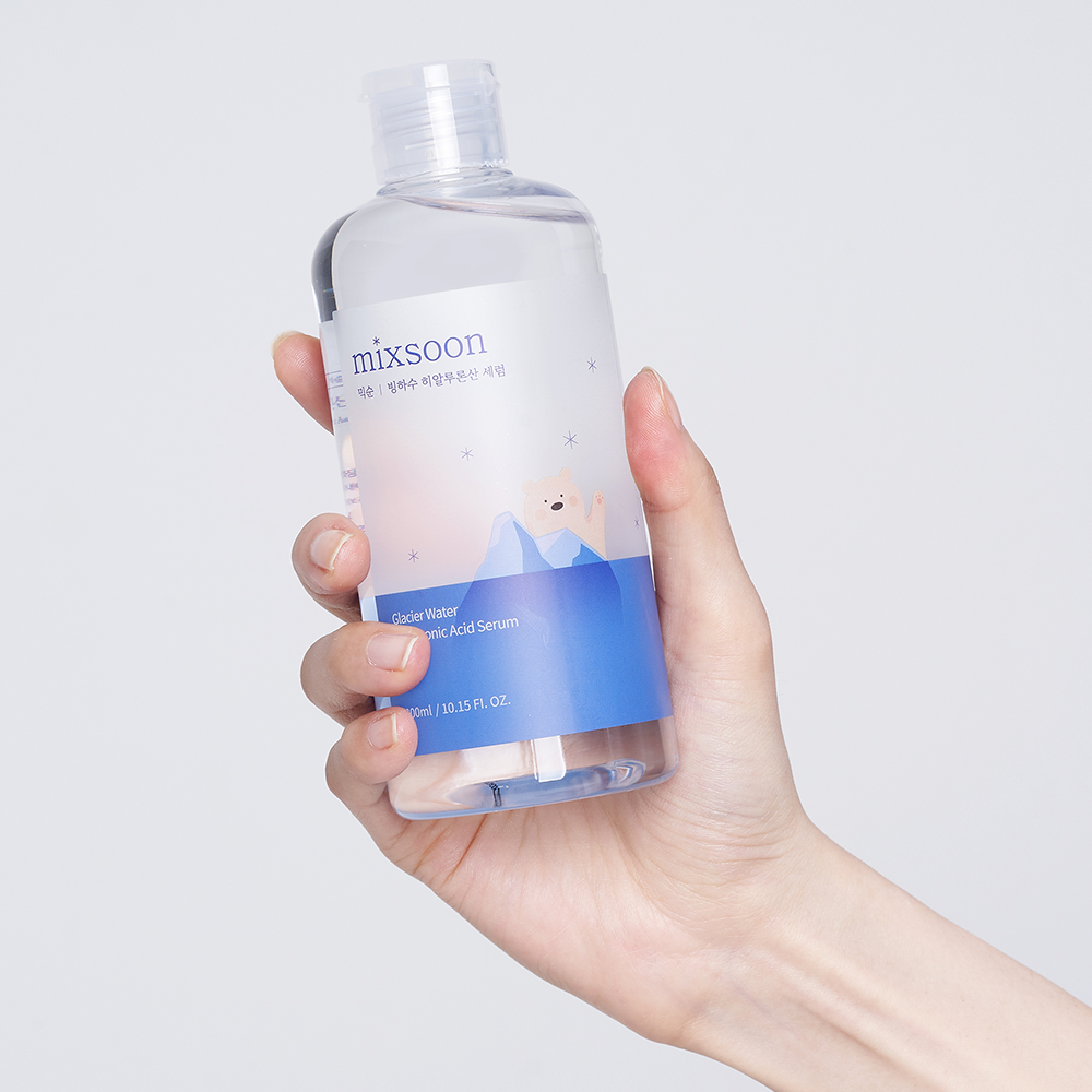 A hand holding a clear bottle of Mixsoon Glacier Water Hyaluronic Acid Serum against a light gray background.