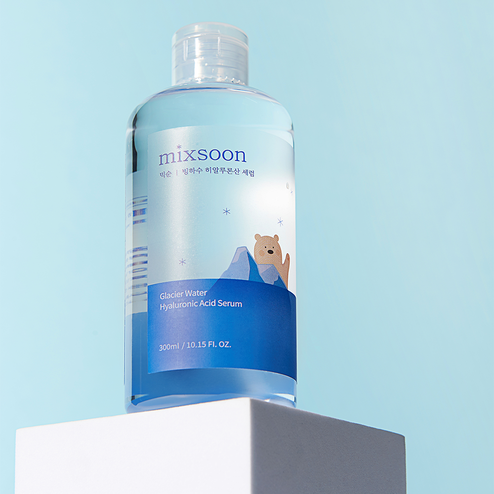 A bottle of mixsoon Glacier Water Hyaluronic Acid Serum with a blue and white label featuring a cartoon bear, displayed on a white pedestal against a light blue background.