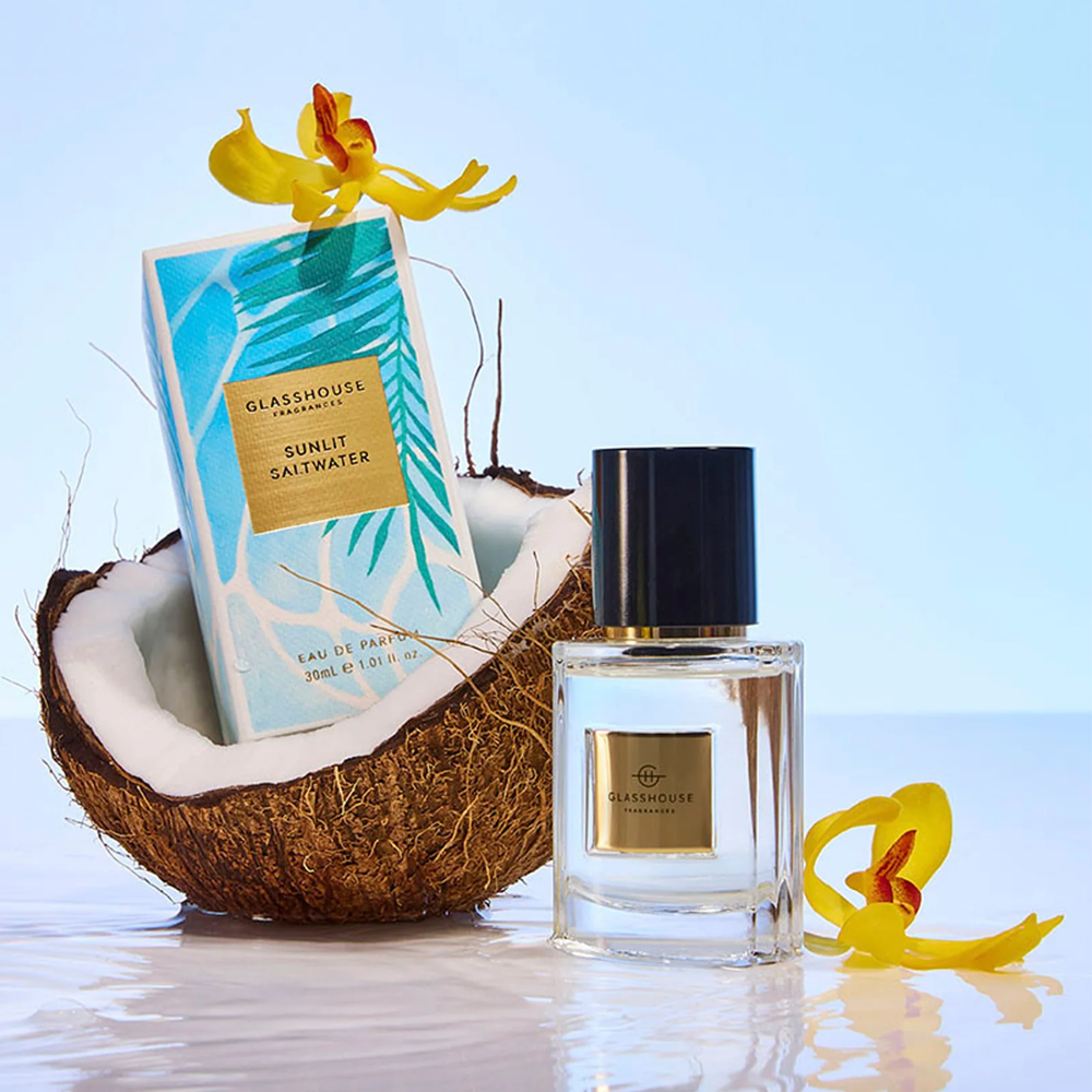 Glasshouse Sunlit Saltwater perfume bottle and packaging with a coconut and flowers on an aquatic light blue background.