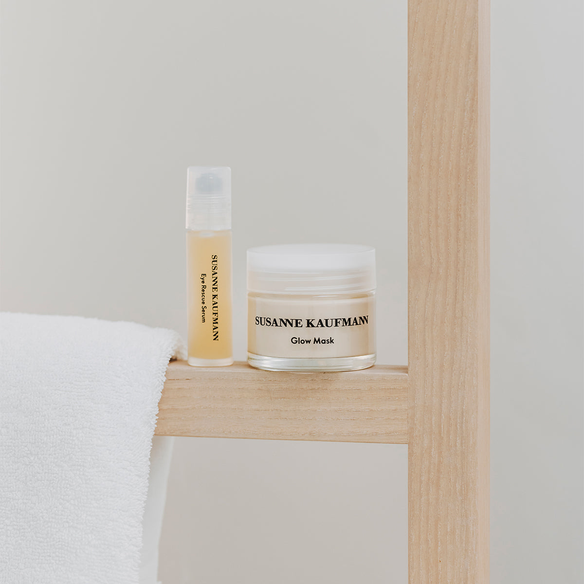 Susanne Kaufmann Glow Mask sitting on a wood structure next to the Eye Rescue Serum and a white towel